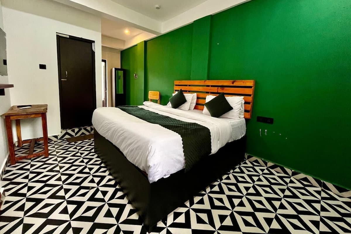 A hotel room with a bed, green walls, and a geometric patterned floor.