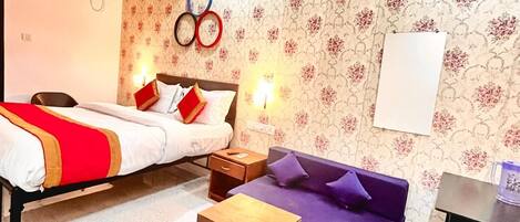 A hotel room with a bed, a sofa, a small table, and a wall clock.