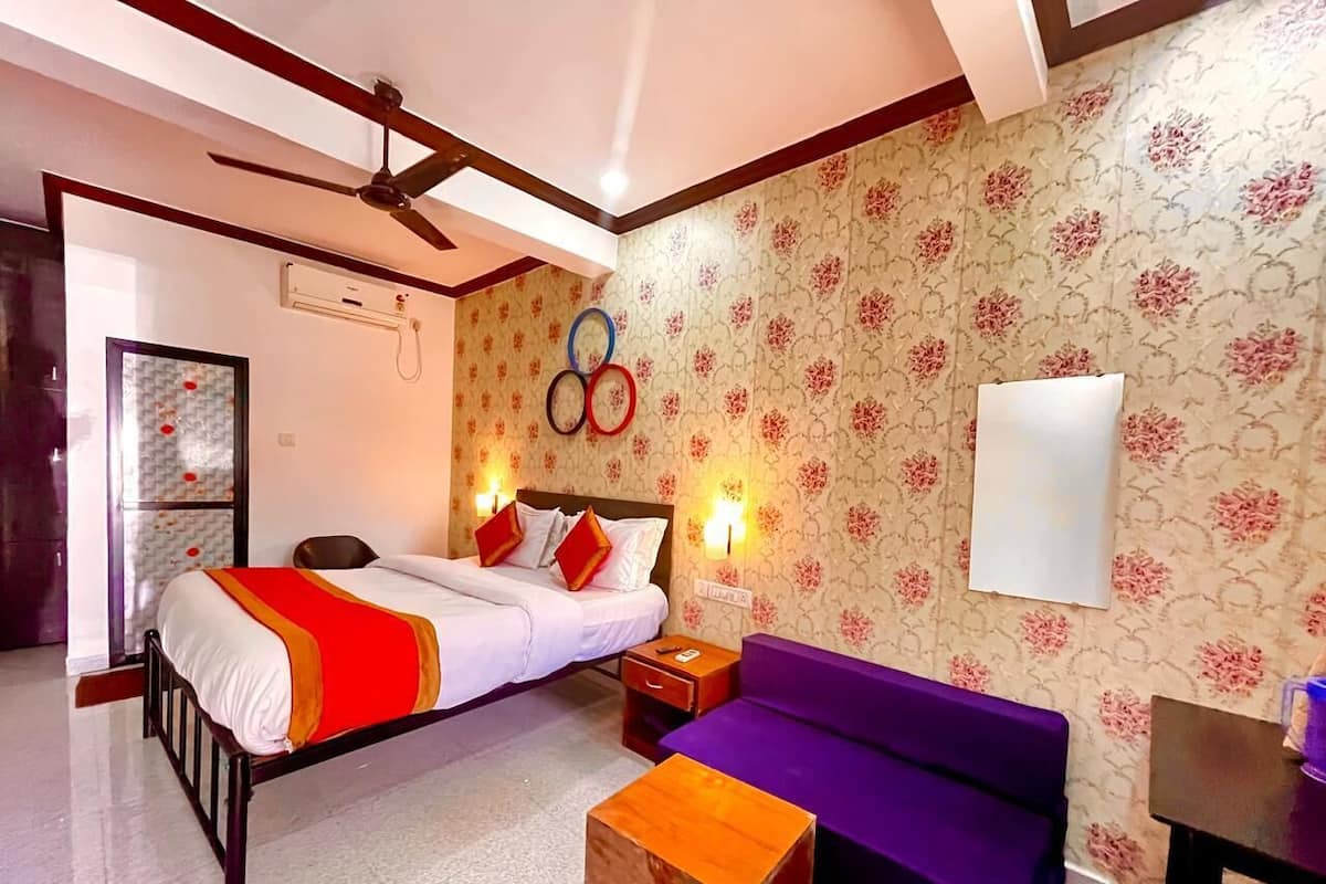 A hotel room with a bed, a purple sofa, a wooden nightstand, and a wall-mounted air conditioner.