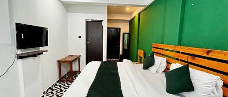 A hotel room with a bed, a TV, a small table, and a green accent wall.