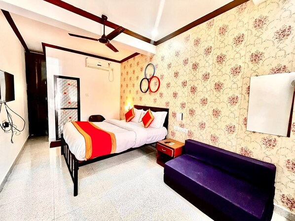 Une chambre à coucher avec un lit, un canapé violet, un ventilateur de plafond et un mur orné des anneaux olympiques.