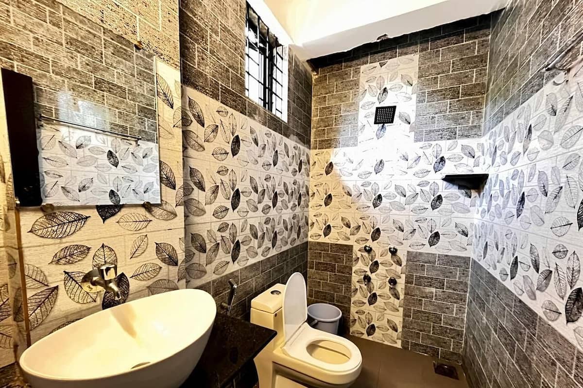A bathroom with a large oval sink, a toilet, and a shower area. The walls are tiled with a leaf pattern.