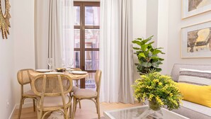Un coin repas avec des chaises en osier, une table en verre et un vase rempli de fleurs jaunes.