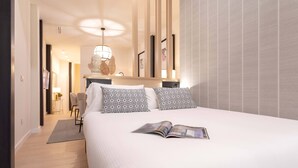 Une chambre d’hôtel moderne avec un grand lit, une lampe de lecture et une vue sur le couloir.