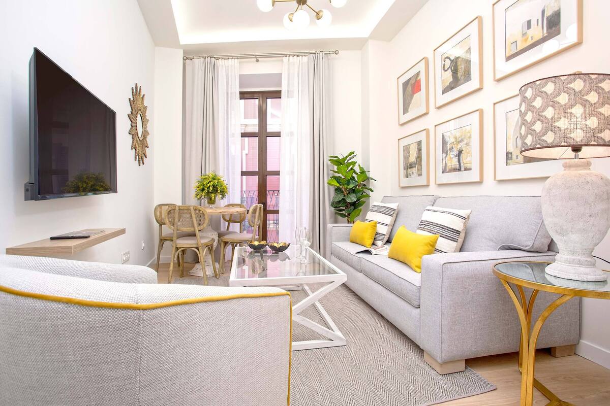 A modern living room with a sofa, a glass coffee table, a TV mounted on the wall, and framed pictures on the wall.
