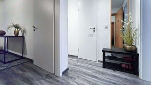 A hallway with a wooden floor, white walls, a door, and a small table with a plant. - Alpha Apartments: Central 1BR, Near Main Station (Essen)