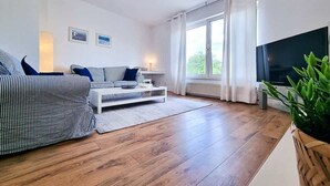 Un salon moderne avec un canapé, une table basse, un téléviseur et une grande fenêtre avec des rideaux.