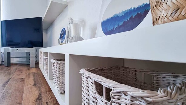 Un salon moderne avec un téléviseur à écran plat, des paniers en osier et un tableau accroché au mur.