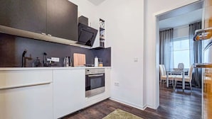 A modern kitchen with white cabinetry, a built-in oven, and a dining area with a table and chairs.