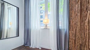 A room with a large window, a mirror, and a lamp.