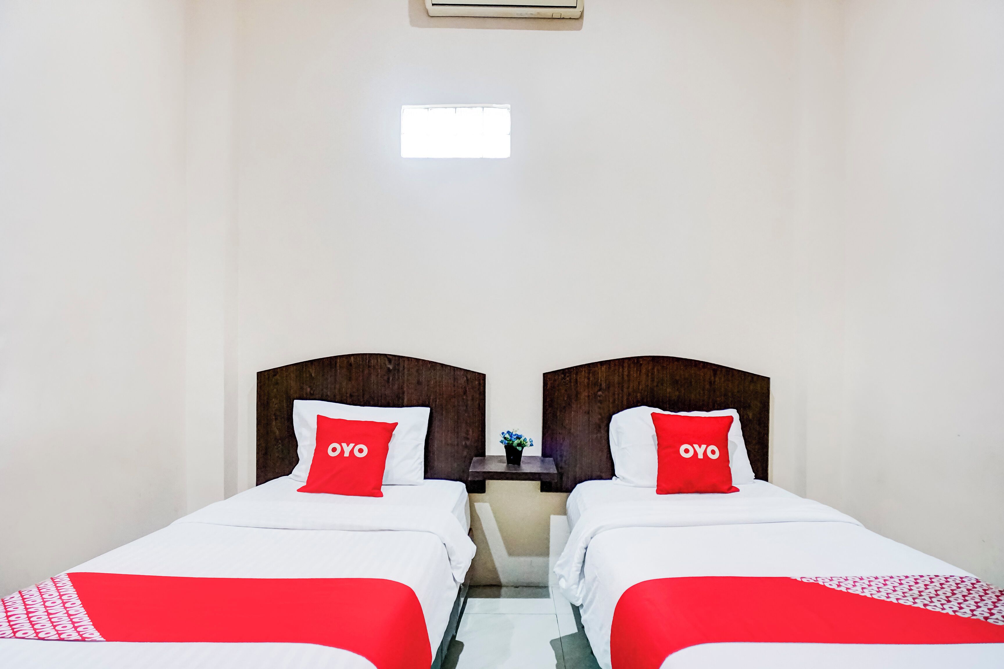 A hotel room with two beds, each with a red pillow and a white bedspread.