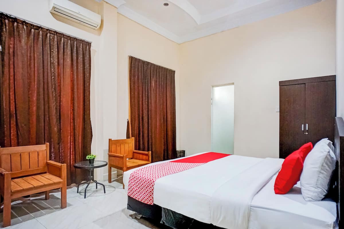 Une chambre d’hôtel avec un lit, deux chaises en bois, une petite table ronde avec une plante et une armoire.