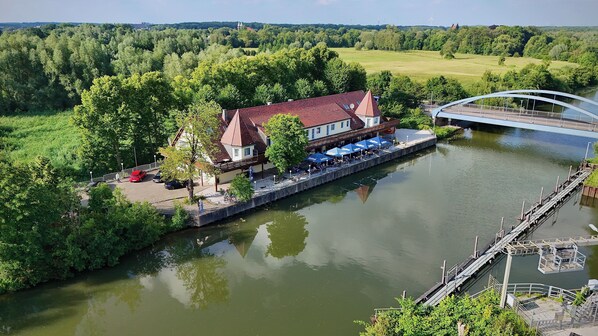 A riverside hotel with a dock, a bridge, and a view of the surrounding greenery. - Bootshaus Hamm (Hamm)