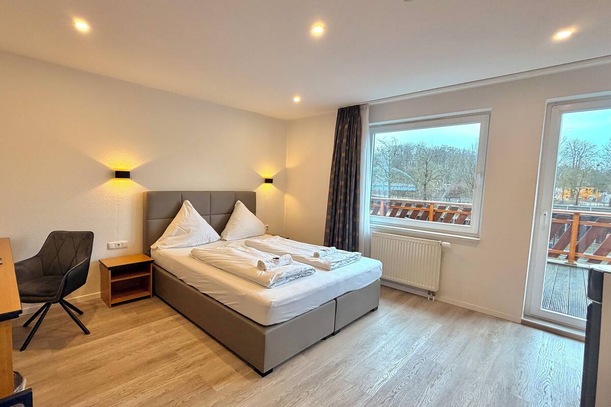 A hotel room with a bed, a desk, a chair, and a window with a view of trees.