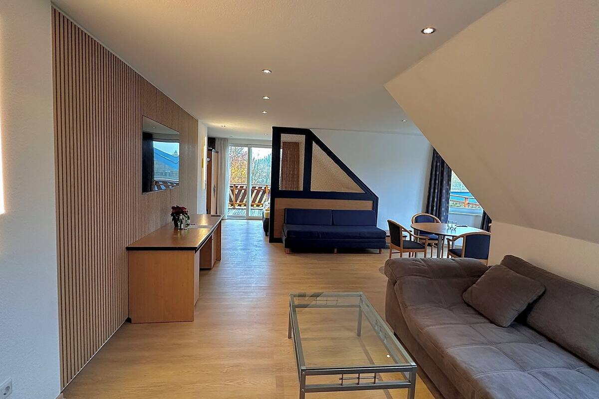 A modern living room with a sofa, a glass coffee table, a dining area with a table and chairs, and a staircase leading to an upper level.