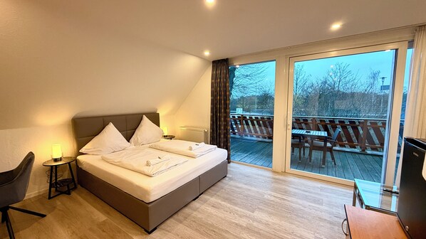 A modern hotel room with a large bed, a desk, and a balcony with outdoor seating. - Bootshaus Hamm (Hamm)