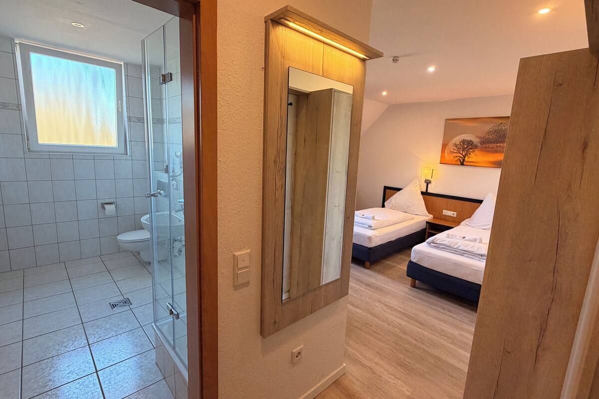 A hotel room with a shower, a bed, a bedside table, and a painting on the wall.