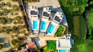 Vista aérea de una propiedad con varias piscinas, un jardín ajardinado y un edificio con paneles solares.