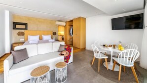 Una habitación de hotel moderna con sofá, una mesa de comedor con sillas, un televisor montado en la pared y un armario.
