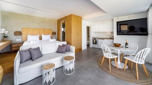 Una habitación de hotel moderna con una cama grande, un sofá, un comedor con sillas, una cocina y un televisor.