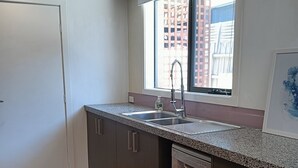 A kitchen with a built-in dishwasher, a window with a view of buildings, and a piano-patterned rug. - Coastal charm, spacious townhouse Ideal for families or groups of up to 8 (Aspendale)