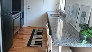 A modern kitchen with a black refrigerator, stainless steel sink, and a granite countertop. There is a wooden herringbone floor and a black and white rug. - Coastal charm, spacious townhouse Ideal for families or groups of up to 8 (Aspendale)