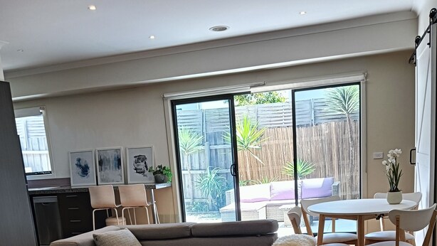 A modern living room with a grey sofa, a white coffee table, and a dining area with a round table and chairs. - Coastal charm, spacious townhouse Ideal for families or groups of up to 8 (Aspendale)