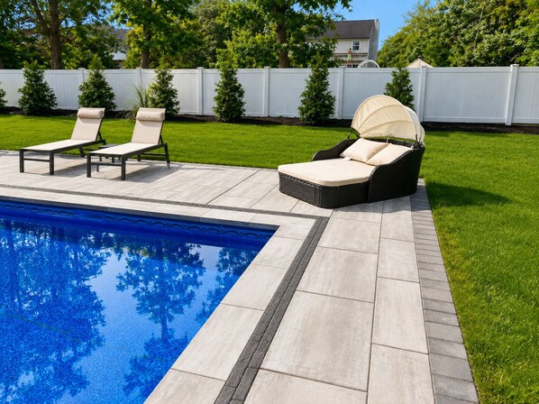 A backyard with a swimming pool, two lounge chairs, and a covered seating area.