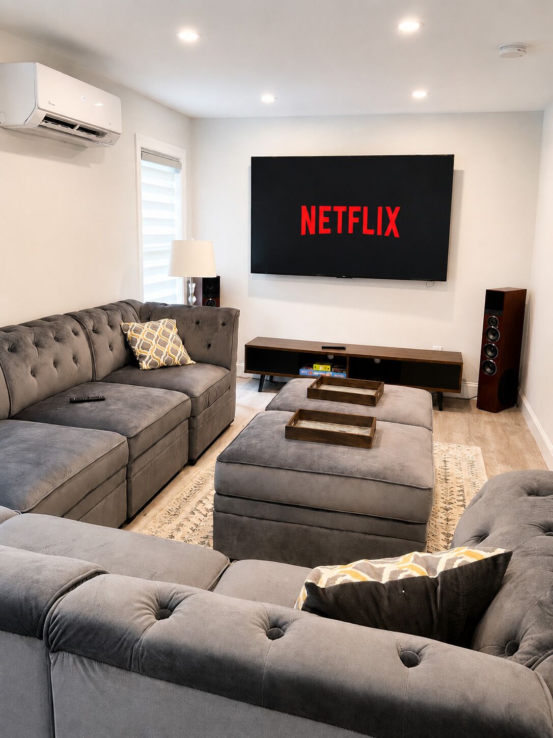 A modern living room with a sectional sofa, a flat-screen TV mounted on the wall, and a wooden entertainment unit.