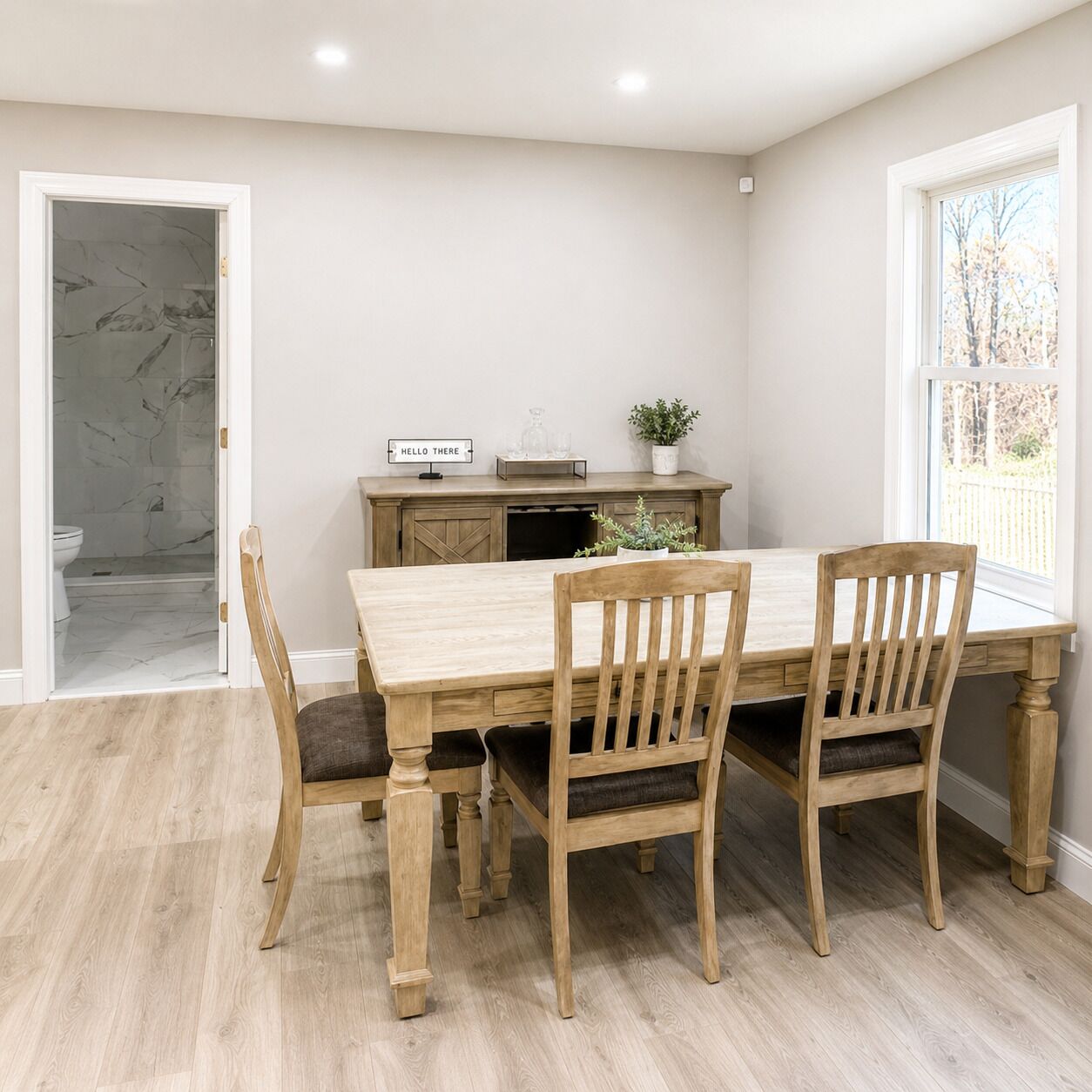 A dining area with a wooden table and chairs, a kitchen area with cabinets and a countertop, and a view of the outdoors through a window.