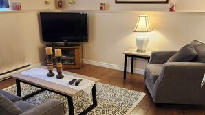 Un salon avec un téléviseur à écran plat, une table basse ornée de bougies, un canapé gris, un tapis à motifs et un tableau accroché au mur.