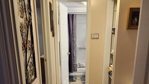 Un couloir étroit, orné d’un tapis à motifs, avec un appareil électroménager blanc et une porte donnant sur une salle de bain.