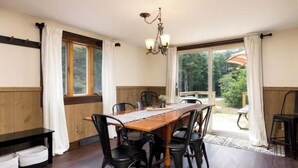 A dining area with a wooden table and black chairs, a chandelier, and a view of the outdoors through large windows. -  Private Adirondack Bear Retreat  (Athol)