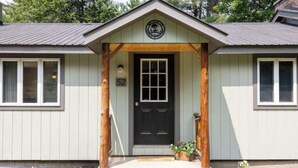 A building with a dark front door, a porch with wooden posts, and a small number '52' sign above the door. -  Private Adirondack Bear Retreat  (Athol)