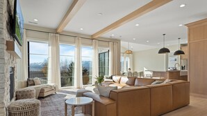 A modern living room with a large sectional sofa, a small round table, and a view of a mountainous landscape through large windows.