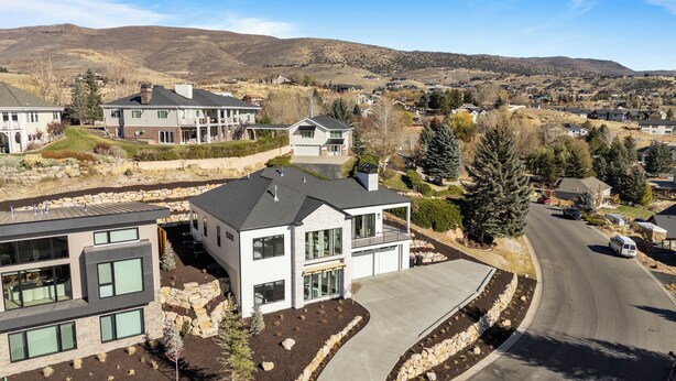 A modern residential area with houses featuring large windows, stone foundations, and a mix of flat and sloped roofs.
