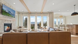 A modern living room with a fireplace, a large sectional sofa, and a dining area with a view of the mountains.