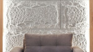 A room with a textured stone wall, a grey sofa, and a wooden floor. - ApartHotel by PikHost (Shkodër)
