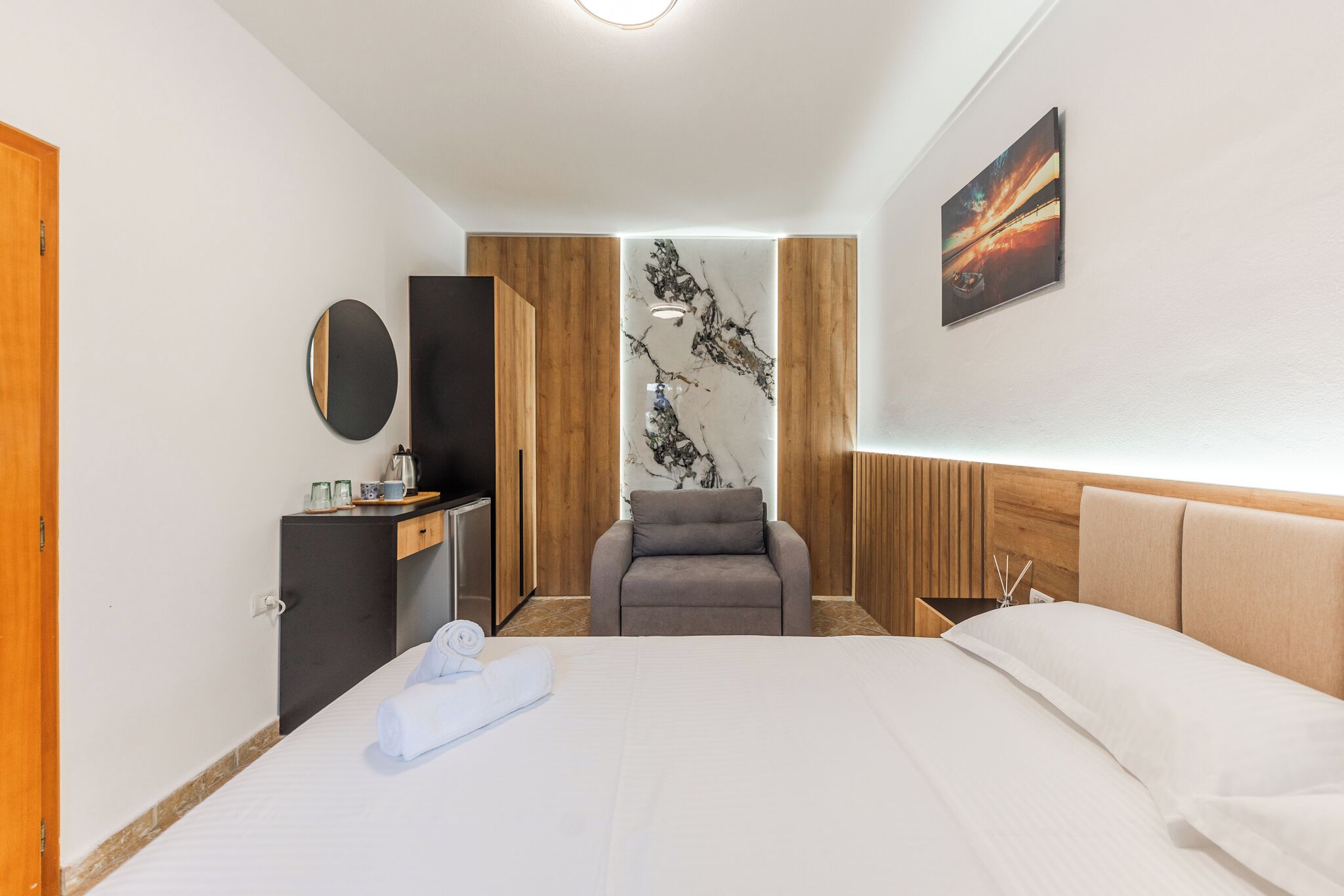 A hotel room with a bed, a desk, a chair, a wardrobe, and a wall with a painting.
