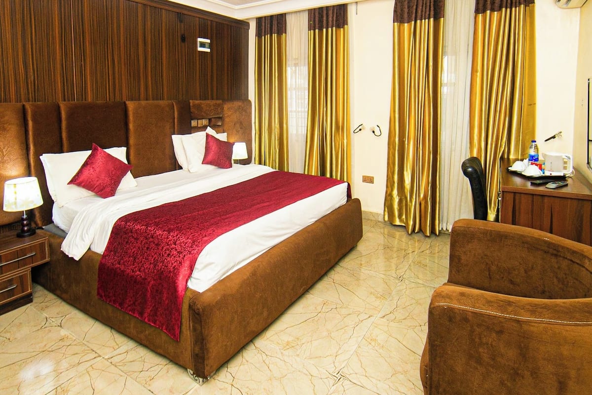 A hotel room with a large bed, a wooden headboard, a marble floor, and a brown armchair.