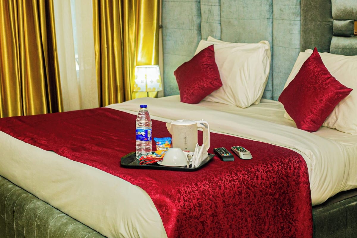 A hotel room with a large bed, red and white bedding, a water bottle, a tray with snacks, a remote control, and a cup.