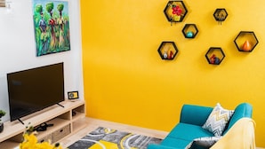 A living room with a teal sofa, a flat-screen TV, and a yellow wall. - BALACASA - THE GETAWAY (Balata)