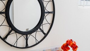 Ein Badezimmer mit einem weißen Waschbecken, einer Rückwand aus Mosaikfliesen, einem runden Spiegel und einem Korbwäscher mit roten Blumen.