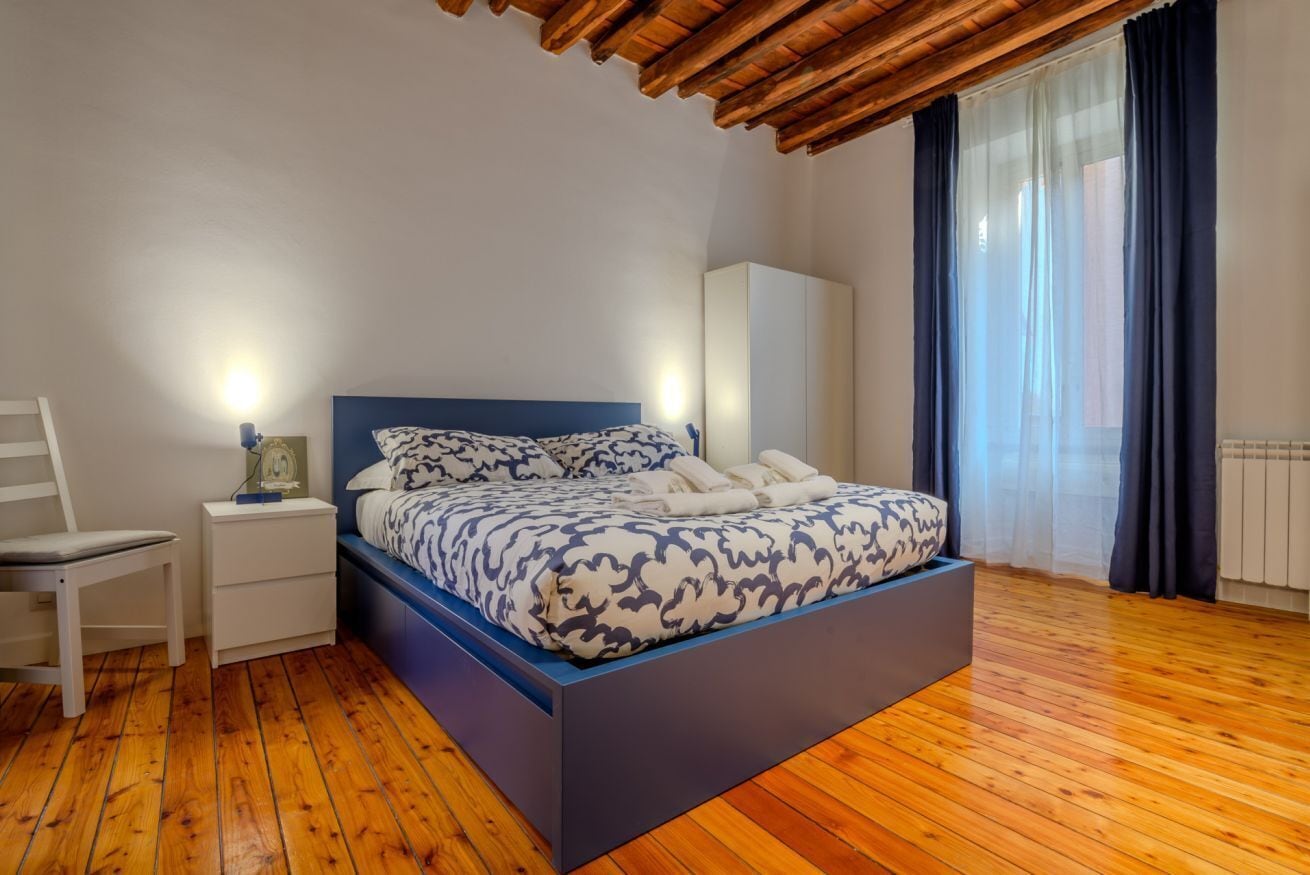 A bedroom with a bed, bedside table, chair, and a window with curtains.