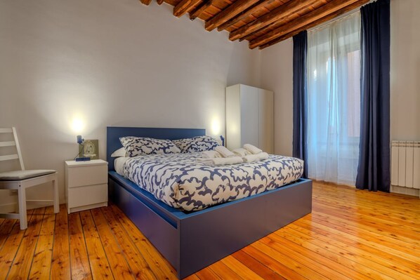 A bedroom with a bed, bedside table, chair, and a window with curtains.