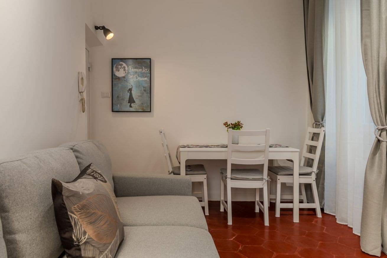 Una sala de estar con un sofá, una mesa de comedor con sillas, un teléfono montado en la pared y un cuadro enmarcado.