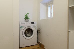 A compact laundry room with a front-loading washing machine, a small potted plant, and a window. - Cozy Flat Orso Navona square (Roma)