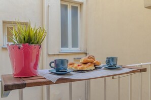 A balcony with a potted plant, two cups, and pastries on a tray.
