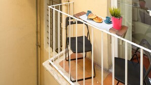 A balcony with a table, chairs, a potted plant, and a window with a view. - Cozy Flat Orso Navona square (Roma)