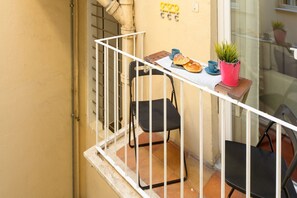 A balcony with a table, chairs, a potted plant, and a window with a view.